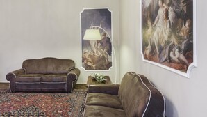 A room with two brown leather sofas, a patterned rug, a lamp, and two large classical paintings on the wall. - San Marco Deluxe Canal View Balcony by Wonderful Italy (Venice)