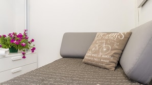A bed with a grey mattress, a pillow with text, a small plant with pink flowers, and a white bedside table. - Accademia Charm 6 by Wonderful Italy (Venice)
