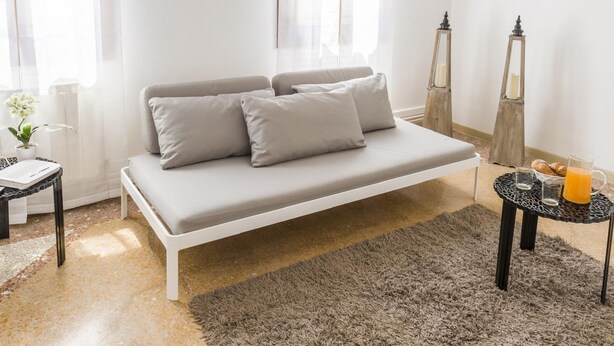 A modern bedroom with a white sofa, a small round table with a drink, and a fluffy rug. - Accademia Charm 6 by Wonderful Italy (Venice)