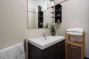 A modern bathroom with a white sink, dark cabinets, a mirror, and a wooden shelf with towels. - San Marco Penthouse 2 by Wonderful Italy (Venice)