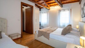 Un dormitorio con techo de madera, una cama con cabecera blanca, una mesita de noche y otra mesita auxiliar.