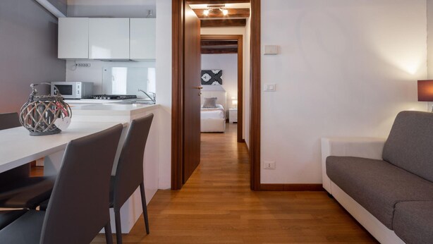 Una cocina moderna con armarios blancos, una mesa de comedor con sillas y piso de madera.