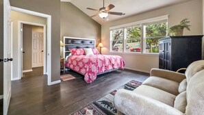A bedroom with a bed, a ceiling fan, a window with a view, and a door.