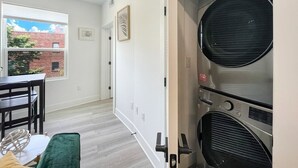 A laundry room with stacked dryers, a table with chairs, and a window with a view of a brick building. - Capitol Hill Scenic Unit with Bright City Views (Washington)