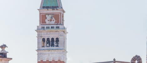 A historic tower with a clock and a statue on top, surrounded by buildings with traditional architecture.