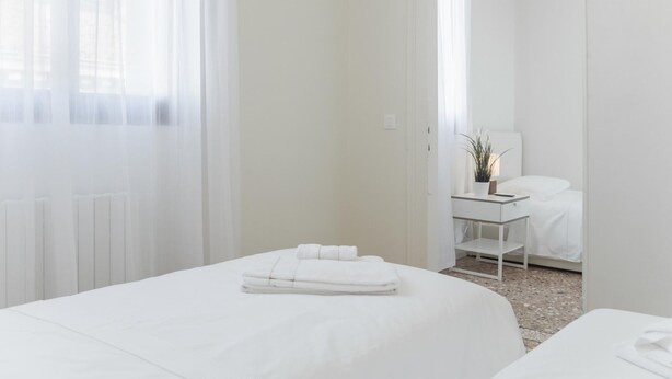 A hotel room with two beds, a bedside table with a lamp, and a view through an open door. - San Marco Penthouse by Wonderful Italy (Venice)