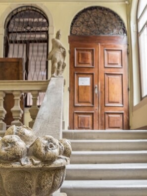 Un escalier en pierre mène à une porte en bois ornée d’une grille métallique décorative.