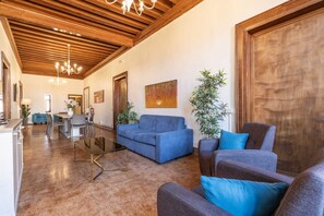A spacious living area with a wooden ceiling, a blue sofa, a glass coffee table, and a dining area in the background. - Tintoretto Style 13 by Wonderful Italy (Venice)
