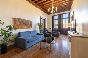 A living room with a sofa, a coffee table, a chandelier, and a TV on a wooden cabinet. - Tintoretto Style 13 by Wonderful Italy (Venice)