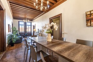 A dining area with a long wooden table, chairs, a vase with flowers, and a chandelier. - Tintoretto Style 13 by Wonderful Italy (Venice)