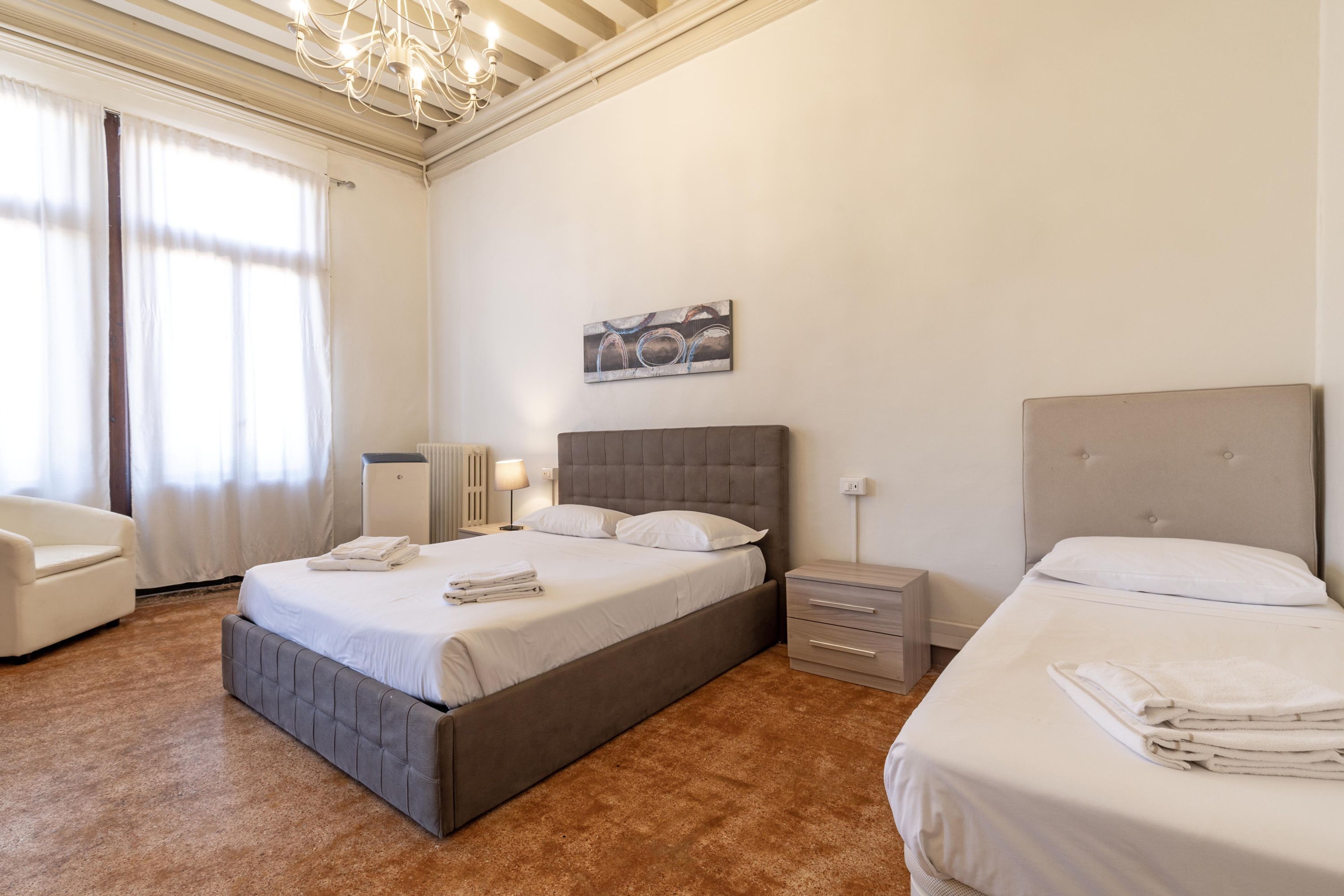 A hotel room with a large bed, a smaller bed, a chair, a nightstand, a lamp, and a painting on the wall.
