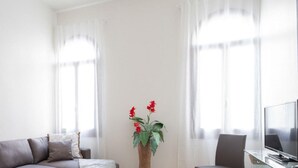 Sala de estar com um sofá cinza, uma televisão e uma planta.
