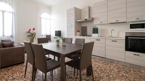 Uma cozinha moderna com armários de madeira clara, uma área de jantar com mesa e cadeiras, e uma sala de estar com sofá e mesa de centro.