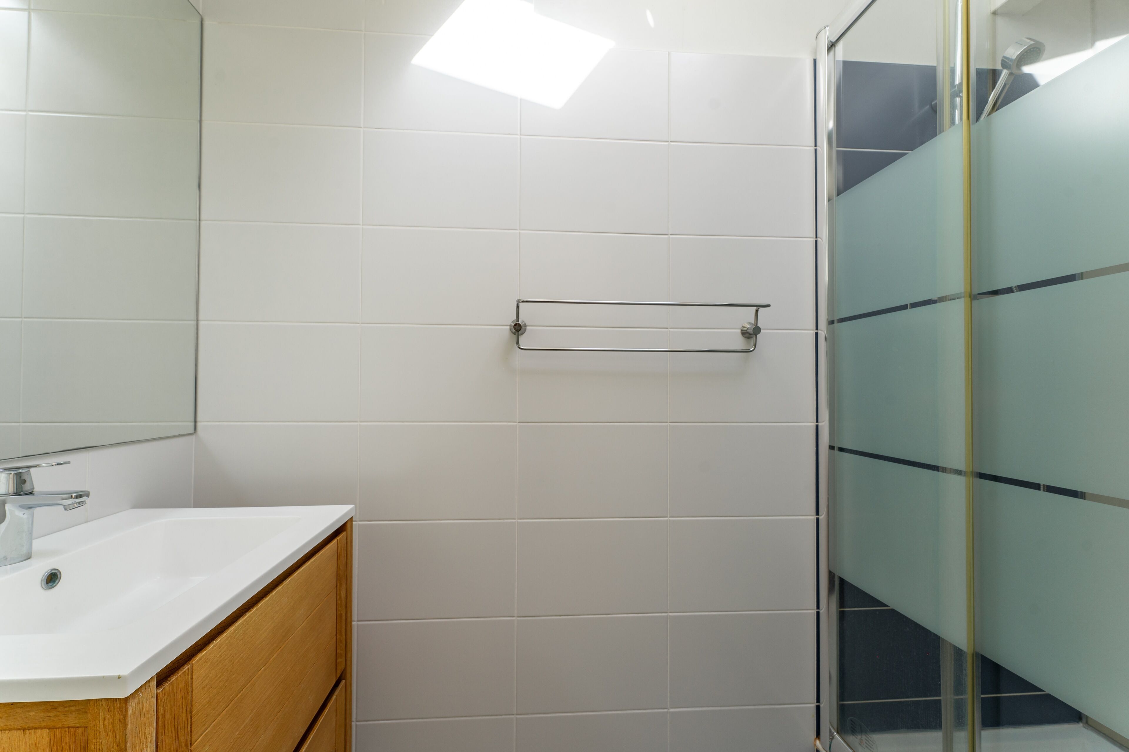 Un baño con lavamanos blanco, mueble de madera y cabina de ducha de vidrio.