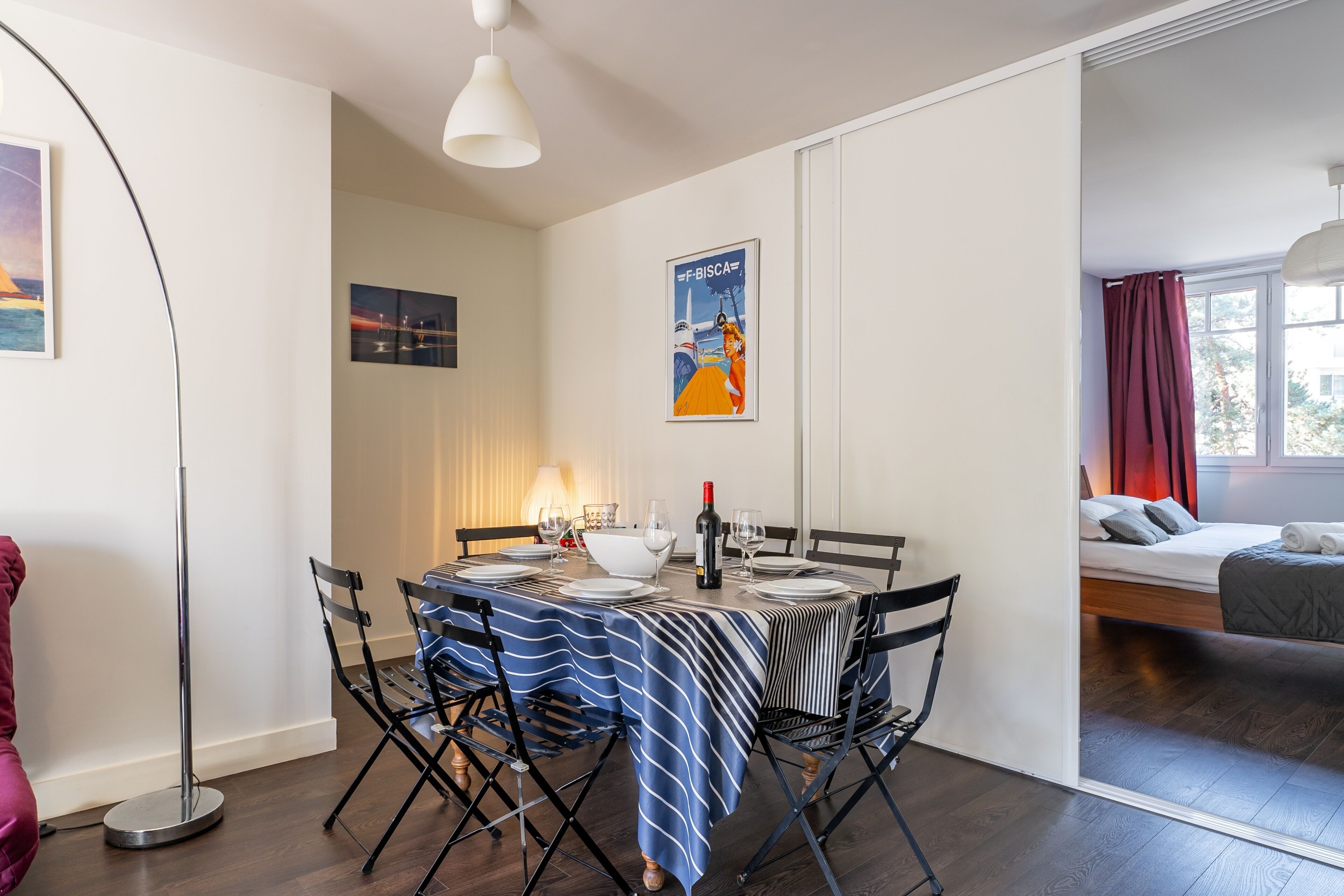 A dining area with a table set for four, a floor lamp, and a poster on the wall.