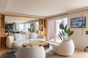 Ein modernes Wohnzimmer mit einer Couch, Sesseln, einem Couchtisch und einem großen Fenster mit Meerblick.
