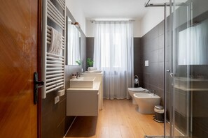 Un baño moderno con puerta de madera, cabina de ducha de vidrio y un amplio ventanal con cortinas translúcidas.