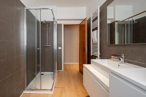Un baño moderno con ducha envuelta en cristal, tocador blanco y espejo grande.