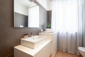 Un baño moderno con un espejo grande, un lavamanos blanco y un inodoro.