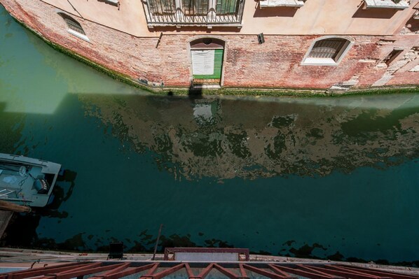 Un canal con una barca atracada a la izquierda, un edificio con puerta verde y una barandilla roja en primer plano.