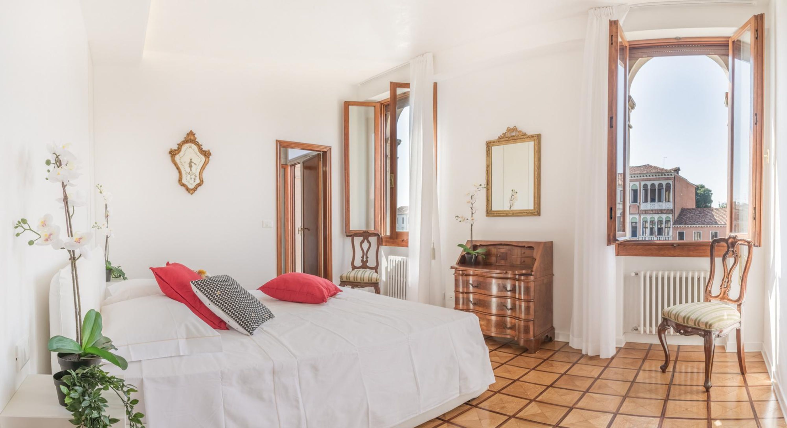 Un dormitorio con cama, cómoda, silla y ventana con vista a edificios.