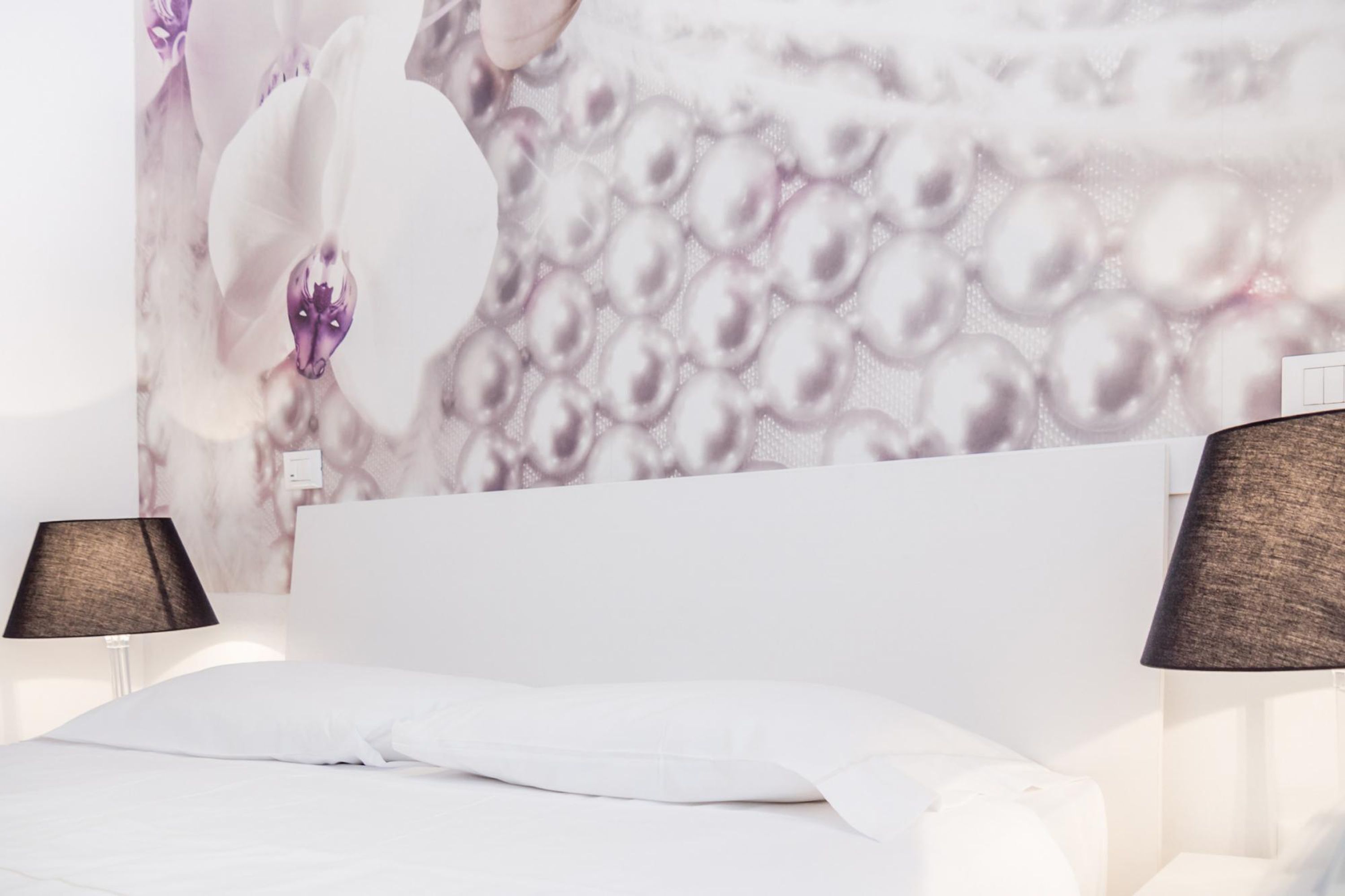 A bedroom with a white bed, two bedside lamps, and a wall with a floral pattern.