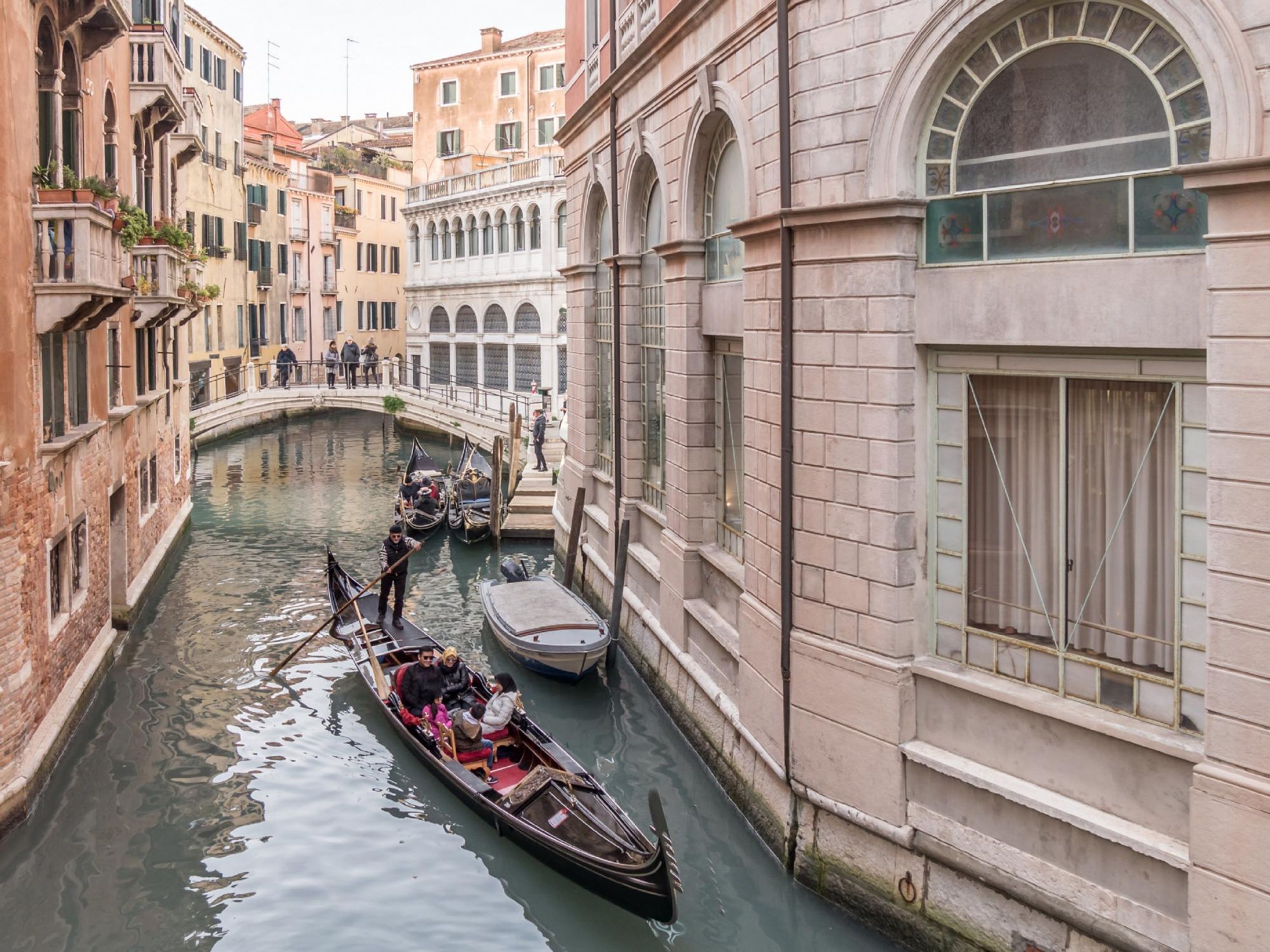 Un canal estrecho con góndolas y un puente, rodeado de edificios históricos con ventanas de arco y balcones.