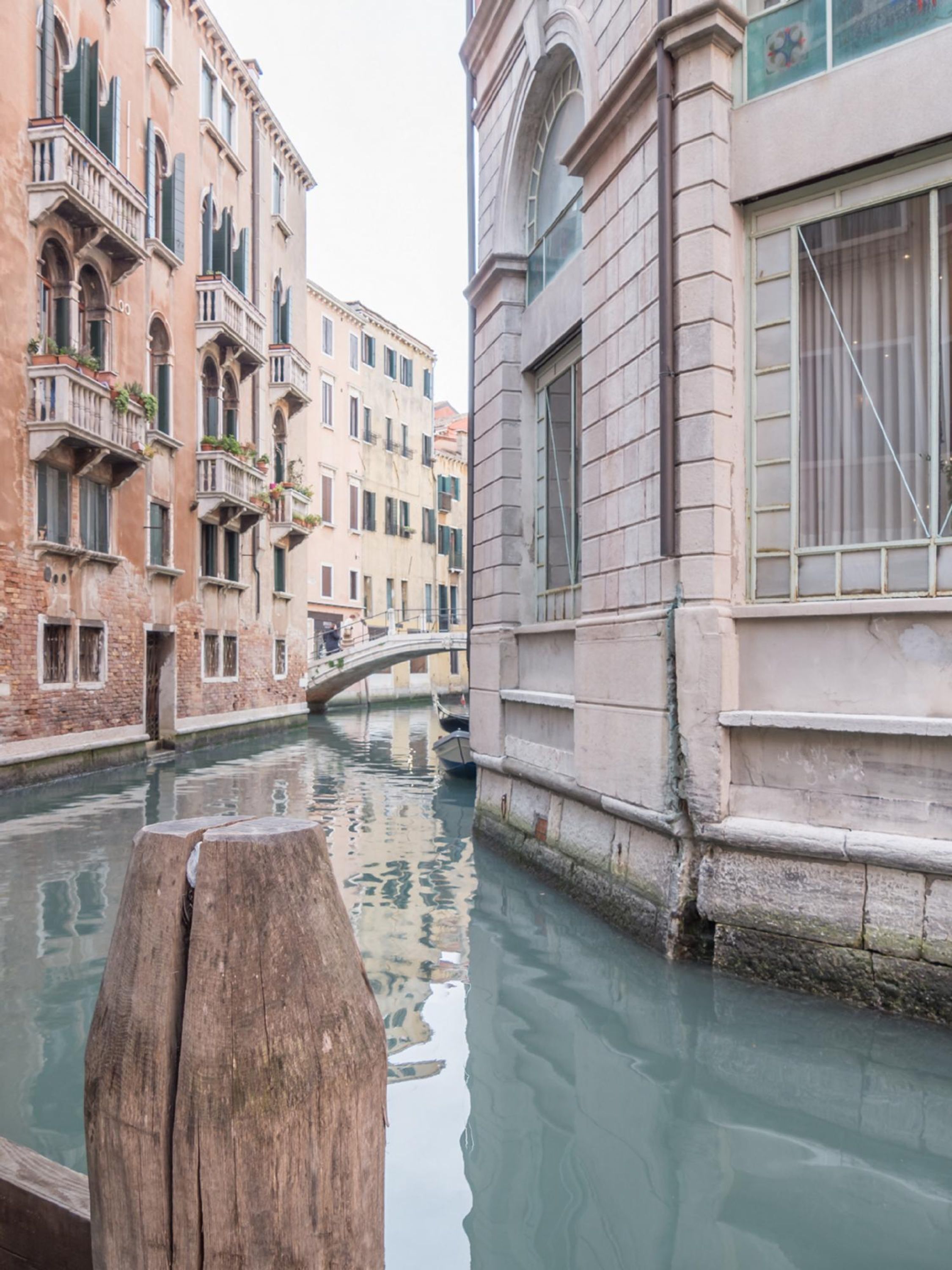 Un canal flanqueado por edificios, un poste de madera en primer plano y un puente al fondo.