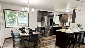 A modern kitchen with a dining area, stainless steel appliances, and a large window. - Cozy Modern Spa ~ Family Fun meets Serene Luxury (Sioux Falls)