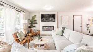 A living room with a fireplace, a sofa, a coffee table, and a chair. - Cozy Modern Spa ~ Family Fun meets Serene Luxury (Sioux Falls)