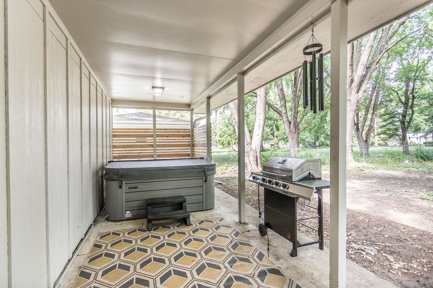 Un espace extérieur abrité comprenant un jacuzzi, un barbecue et un sol à motifs.