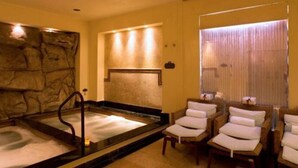 Ett spa-rum med en vägg av sten, ett bubbelbad och tre bekväma fåtöljer.