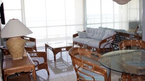 A spacious living area with a glass dining table surrounded by wicker chairs, a sofa with patterned cushions, and a large woven lamp. - Breathtaking Ocean Front View (Carolina)