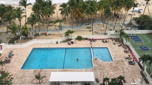 A pool area with two pools, a beach, and palm trees. - Breathtaking Ocean Front View (Carolina)