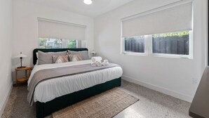 A bedroom with a bed, two bedside tables, a lamp, a window with blinds, and a ceiling light. - Minimalist Luxury in Historic WPB-Great Location Near Town, Beach, Sites! (West Palm Beach)