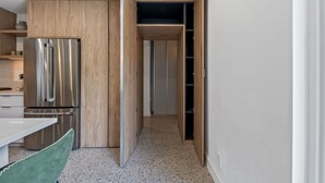 A compact kitchen with a built-in stainless steel refrigerator, wooden cabinets, and a small dining area with a green chair. - Minimalist Luxury in Historic WPB-Great Location Near Town, Beach, Sites! (West Palm Beach)