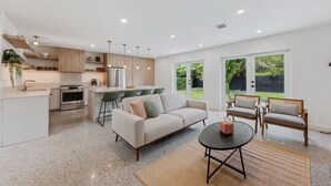 A modern kitchen with a central island, a dining area with a sofa and chairs, and a large sliding glass door leading to a backyard. - Minimalist Luxury in Historic WPB-Great Location Near Town, Beach, Sites! (West Palm Beach)