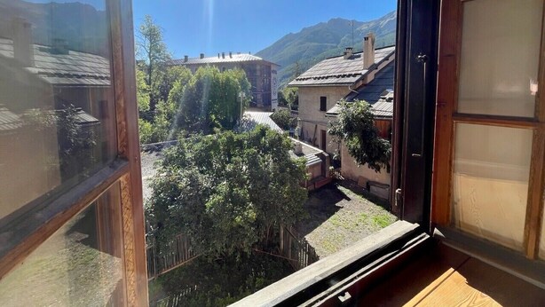 A view from a window overlooking a village with houses and trees, a clear sky, and mountains in the distance.