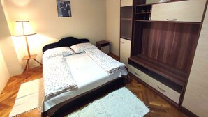 Een slaapkamer met een bed, nachtkastje, lamp, kledingkast en een klein beeldje erop.