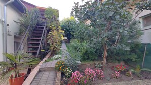 Een woonachtige tuin met een geplaveid pad, potplanten en bloeiende struiken.
