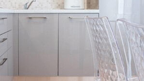 Moderni keittiö, jossa on harmaat kaapit, mikroaaltouuni, leivänpaahdin ja läpinäkyvä tuoli.