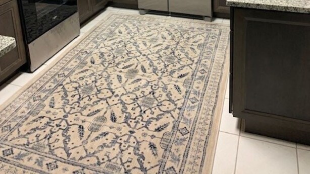 A kitchen with dark wood cabinets, stainless steel appliances, a granite countertop, and a patterned rug.