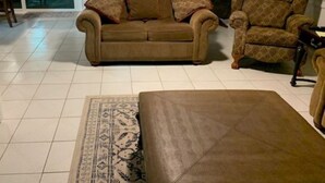A living room with a sofa, armchair, and ottoman. There is a patterned rug on the floor.