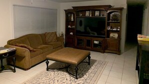 A living room with a brown sofa, a coffee table, a television, and a wooden entertainment center.