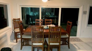 A dining area with a wooden table and chairs, a ceiling fan, and a view through glass doors to the outside.
