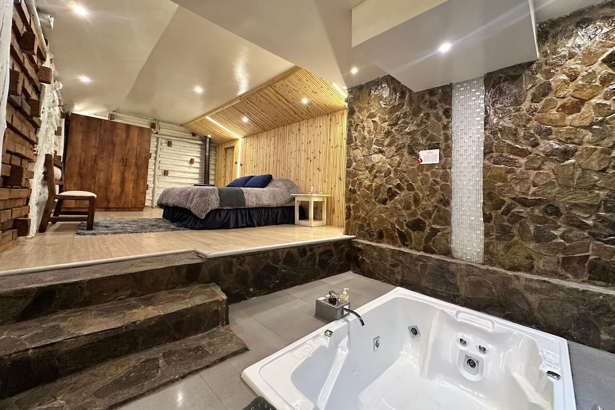 Un dormitorio moderno con una cama grande, una silla de madera y una pared de piedra.