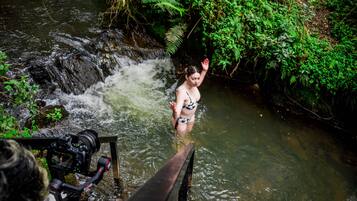 A person in a bikini standing in a stream with a camera on a tripod.