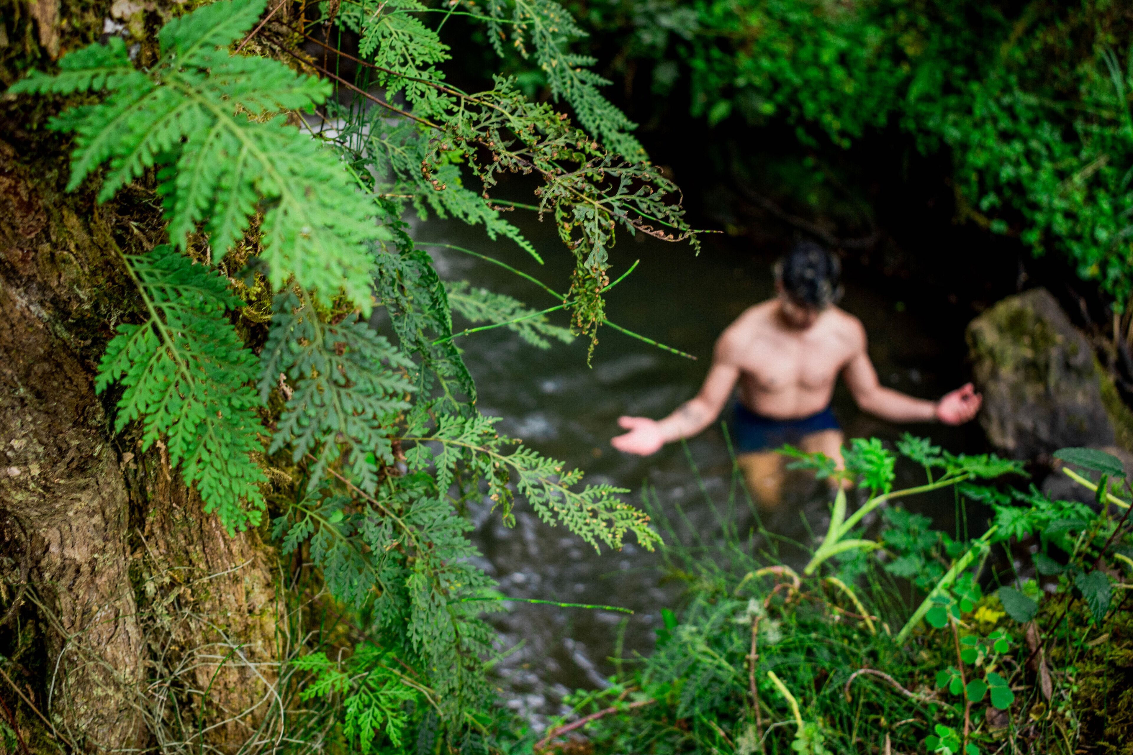 Una persona en traje de baño cerca de una masa de agua natural rodeada de abundante vegetación.