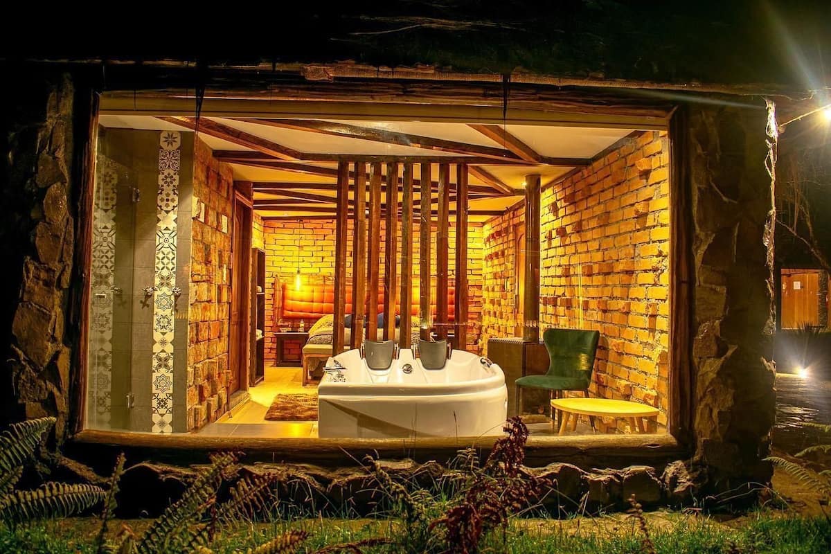 Una cabaña acogedora y rústica con una bañera grande, un sillón verde y detalles de madera.