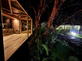 Un edificio moderno integrado entre árboles, con terraza de madera y paredes de piedra.